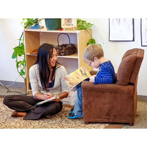 Teacher with pen and notepad sitting with child reading a book