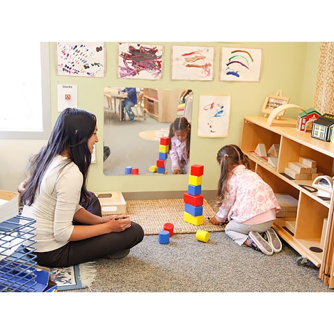 Teacher with pen and notepad observing child playing in block area