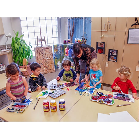 Children painting in art area with assistance from teacher