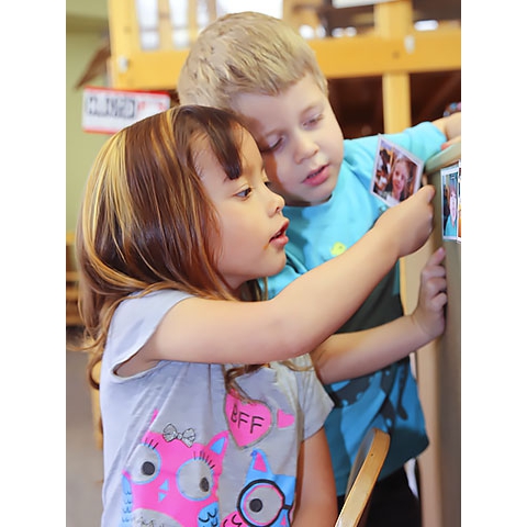 Two children place photos on activity board