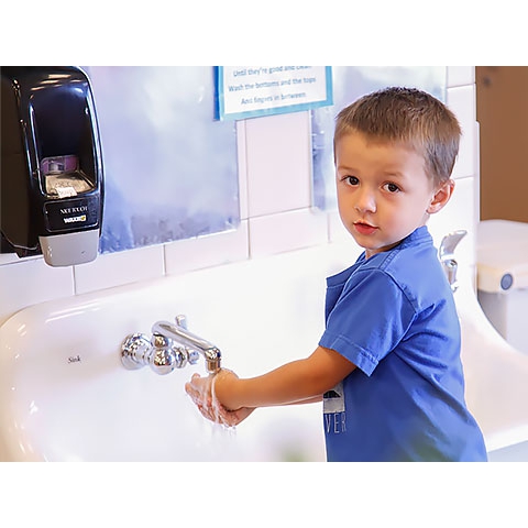 Child washing hands at sink with sample directions on mirror
