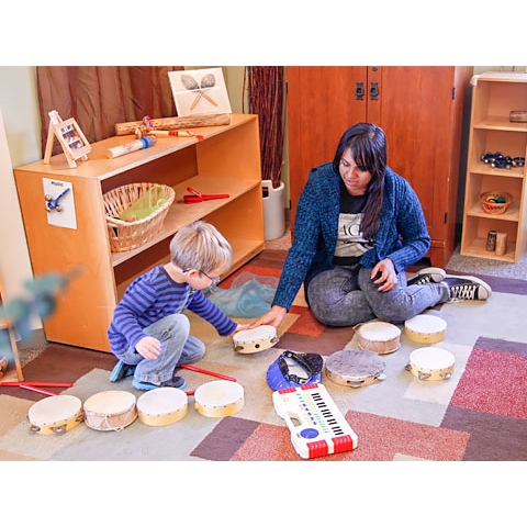 Teacher playing tambourines with child in music area